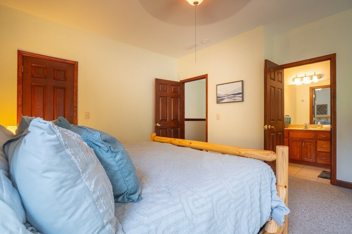 A bedroom with a bed, a wooden headboard, a door, a mirror, and a bathroom visible through an open door.