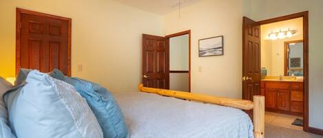 A bedroom with a bed, a wooden headboard, a door, a mirror, and a bathroom visible through an open door.