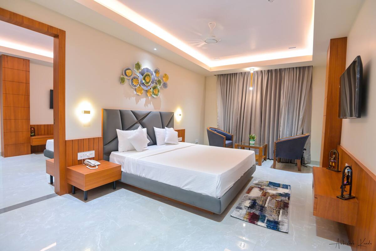 A modern hotel room with a large bed, bedside tables, a desk, a chair, a TV, and a ceiling fan.