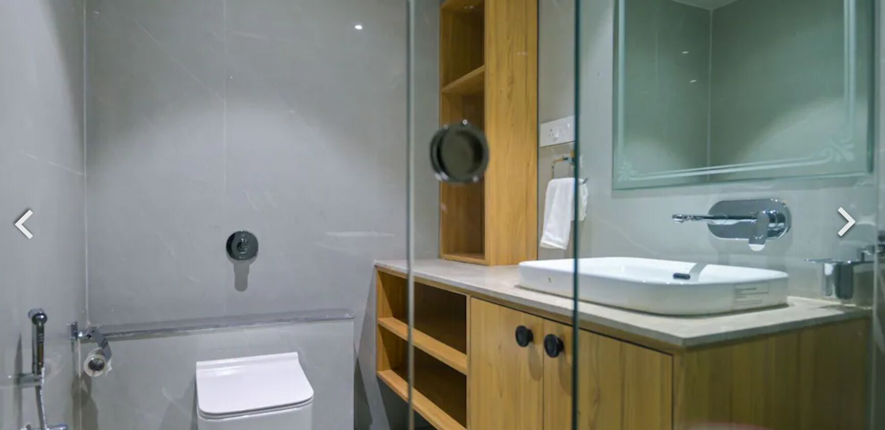 Un baño moderno con cabina de ducha de vidrio, inodoro blanco y tocador de madera con espejo.