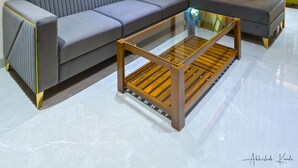 Un salon moderne avec un canapé d’angle gris, une table basse en bois, un ventilateur de plafond et un élément décoratif mural.