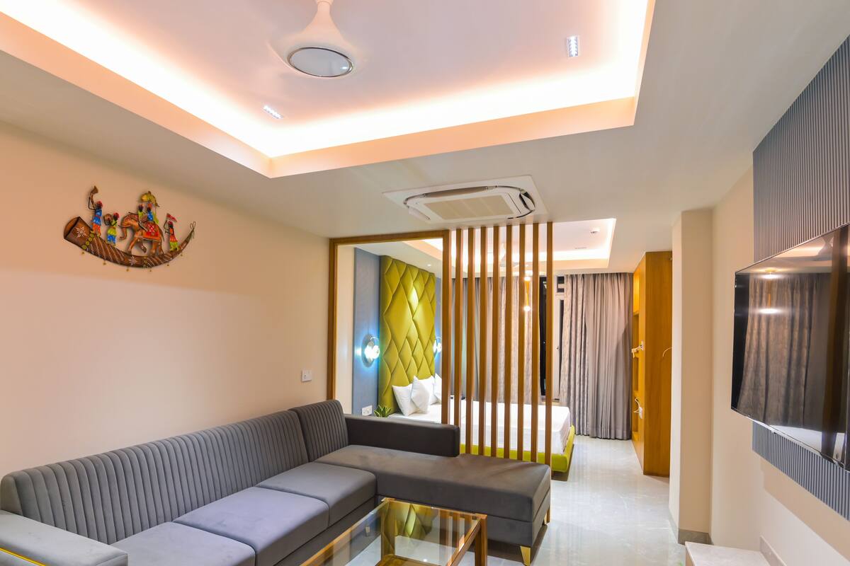 A modern living room with a grey sectional sofa, a decorative wall piece, and a flat-screen TV mounted on the wall.