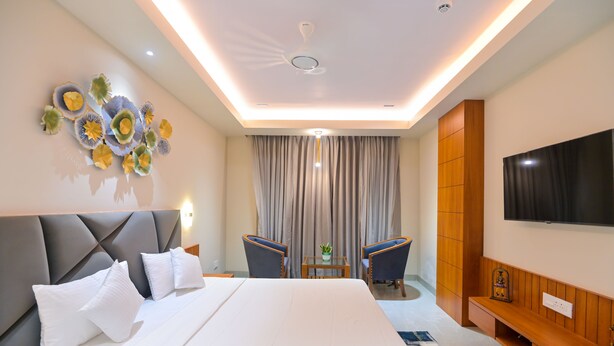 Une chambre d’hôtel dotée d’un grand lit, d’un téléviseur à écran plat fixé au mur, d’un ventilateur de plafond et d’une œuvre d’art décorative.