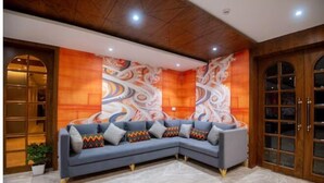 Un salon moderne avec un canapé d’angle gris, un papier peint à motifs colorés et des poutres en bois au plafond.