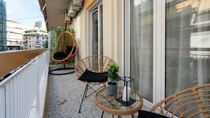 Uma varanda com cadeiras de vime, uma pequena mesa e um vaso de planta.