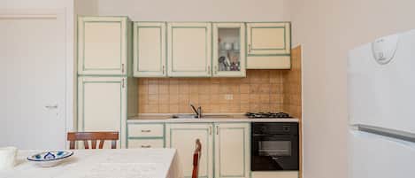 Una cocina compacta con armarios verde claro, un refrigerador blanco y salpicadero de azulejos.