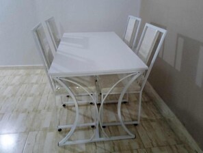 Una mesa blanca de metal con cuatro sillas en una habitación con suelo de baldosas y paredes lisas.