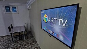 Una habitación con una televisión de pantalla plana que muestra el logotipo de Samsung ART TV, una mesita con sillas y una ventana con vistas.