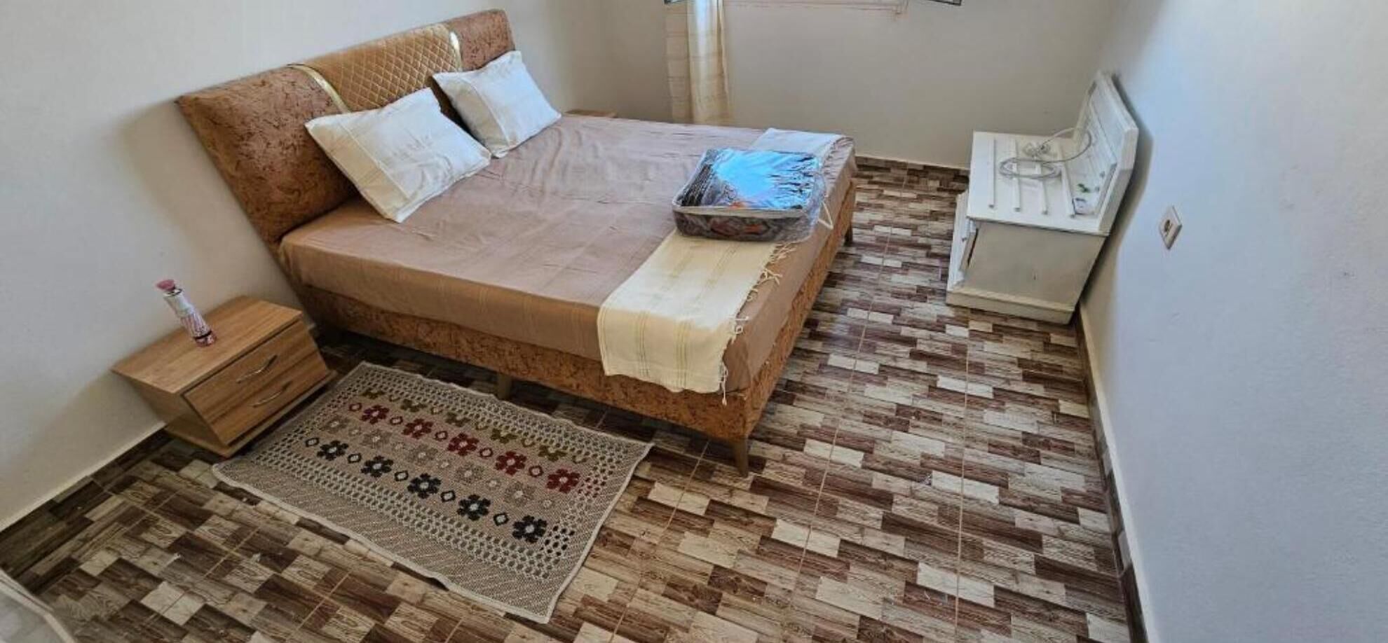 Un dormitorio con cama, mesita de noche, lámpara, alfombra y un calentador.
