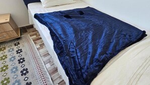 Una cama con una manta azul oscuro, un edredón blanco y una alfombra estampada sobre un piso de madera.