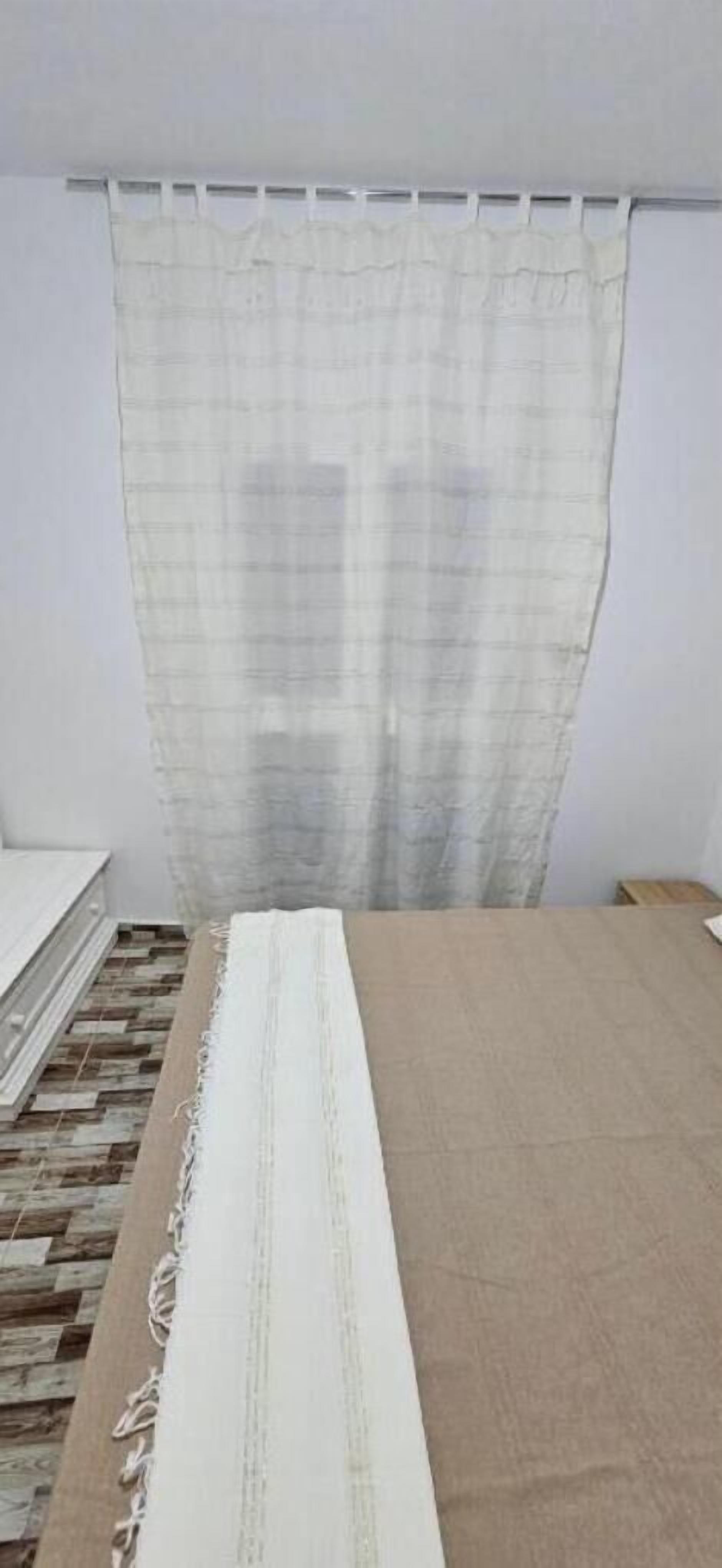 Un dormitorio con una cama, una cortina blanca y una alfombra estampada.