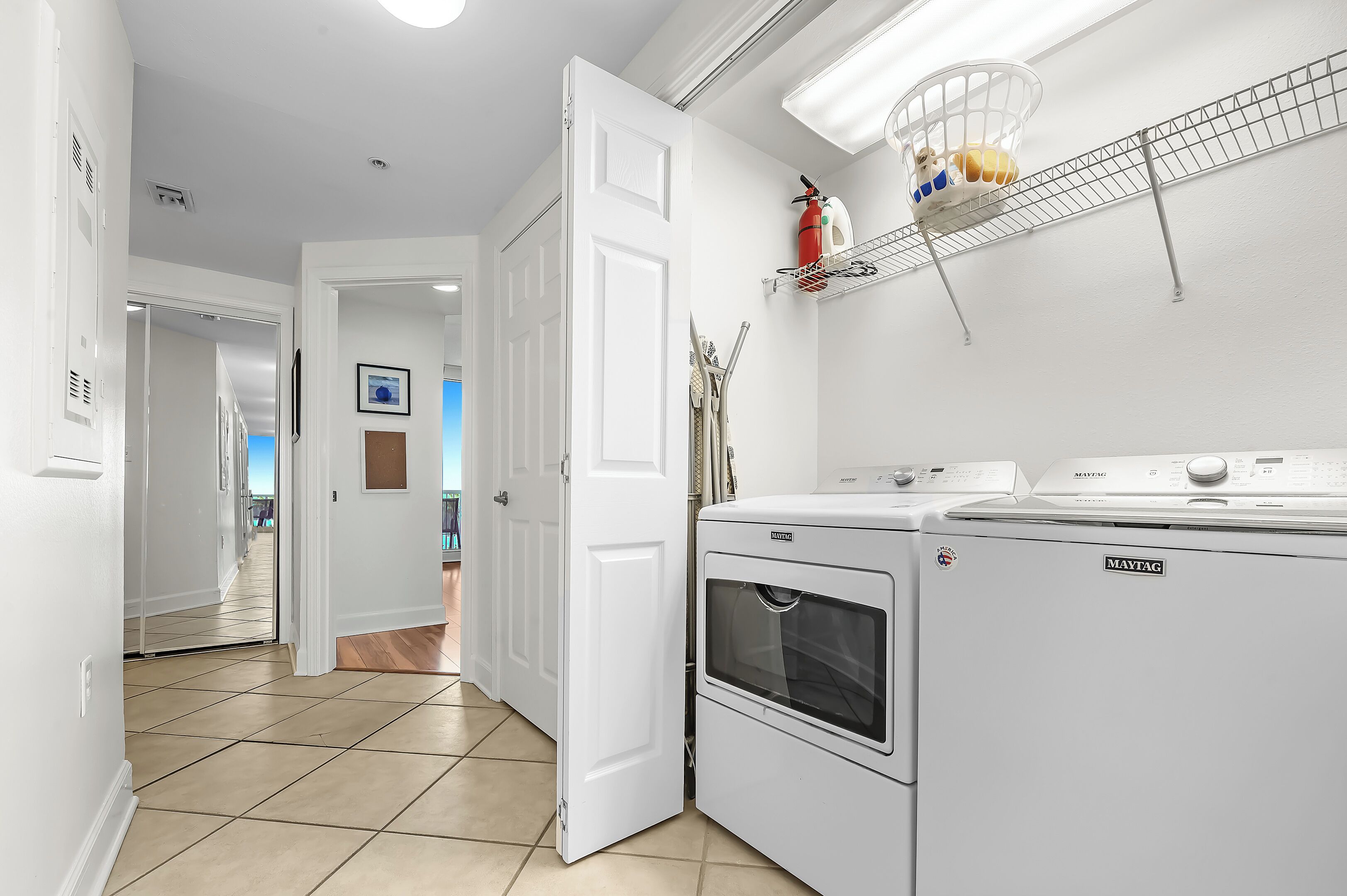 A laundry room with a Maytag washer and dryer, a white door, and a ceiling-mounted shelf with cleaning supplies.