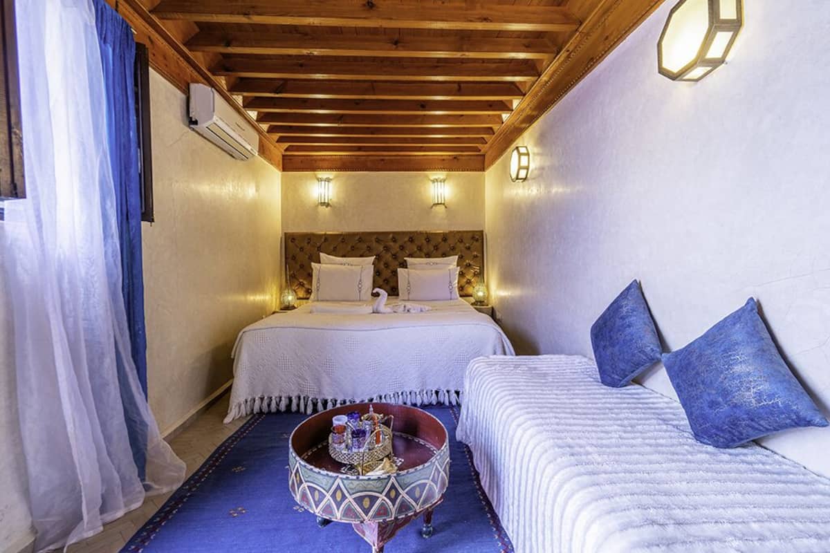 A cozy room with a bed, a small round table with a decorative item, and a sofa with cushions.