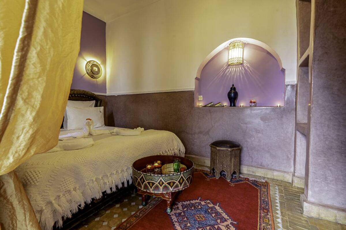 A traditional Moroccan room with a bed, a decorative bowl, a small table, and a wall-mounted shelf.