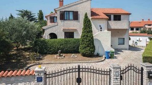 Una casa a due piani con facciata in pietra, tetto in tegole e ingresso protetto da un cancello.