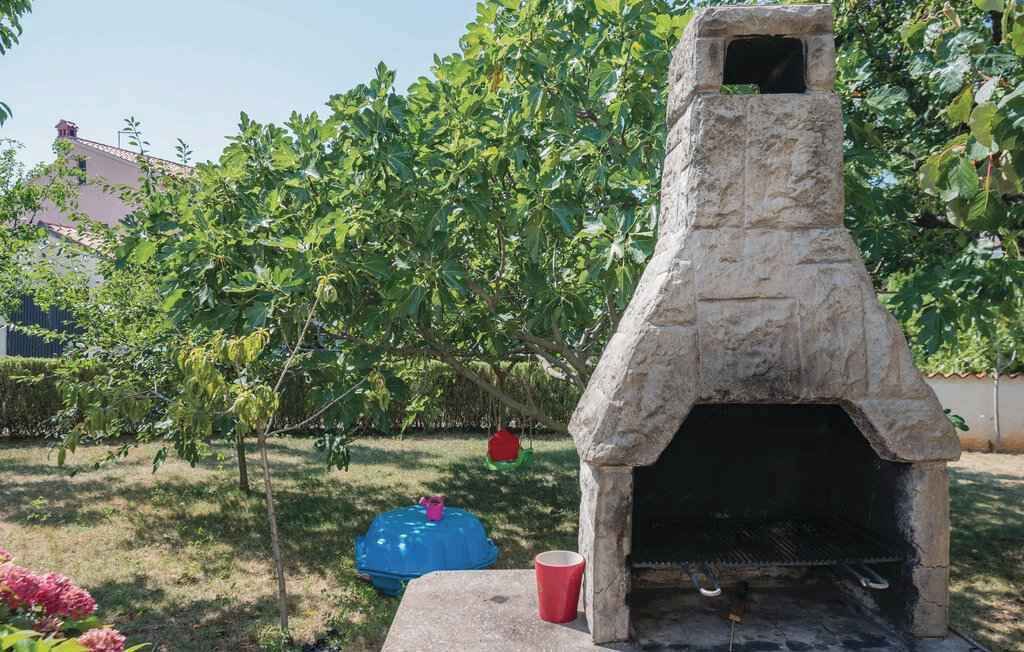 Een buitenoven van steen voor pizza, in een tuin met een boom en een blauwe bak.