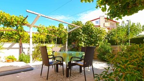 Een buitenpatio met een tafel en stoelen, omgeven door groen en een pergola.