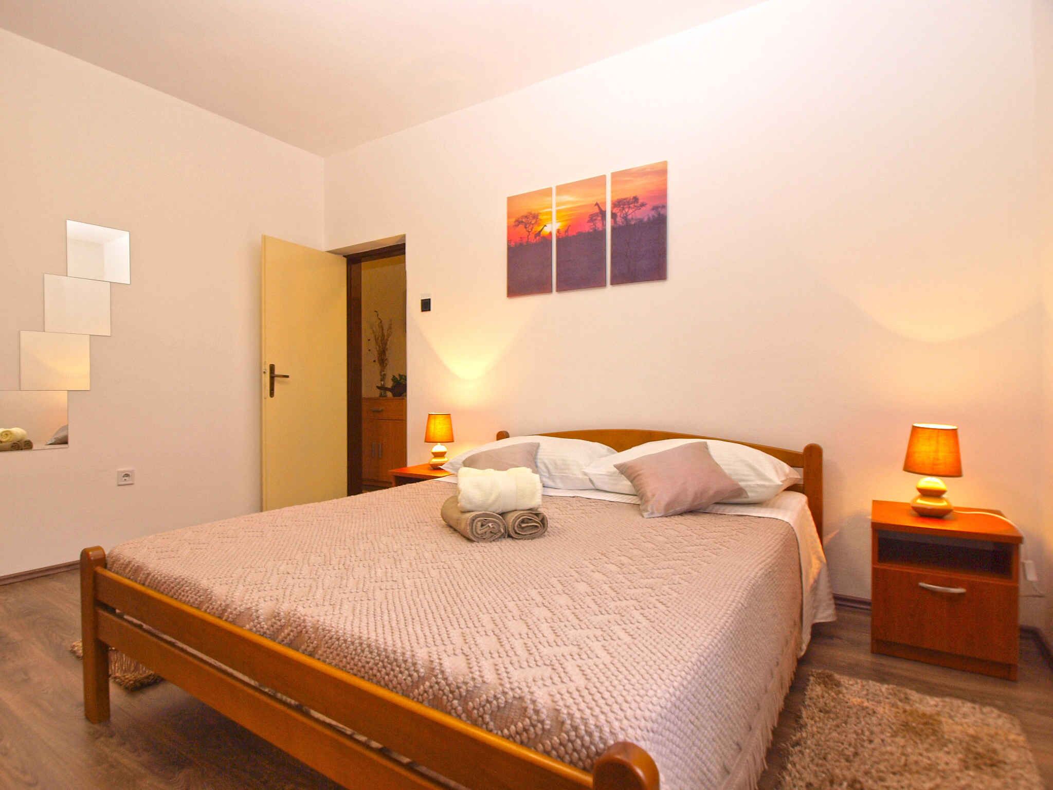 A neatly made bed with a wooden frame, two bedside lamps, a wall-mounted picture, and a door leading to another room.