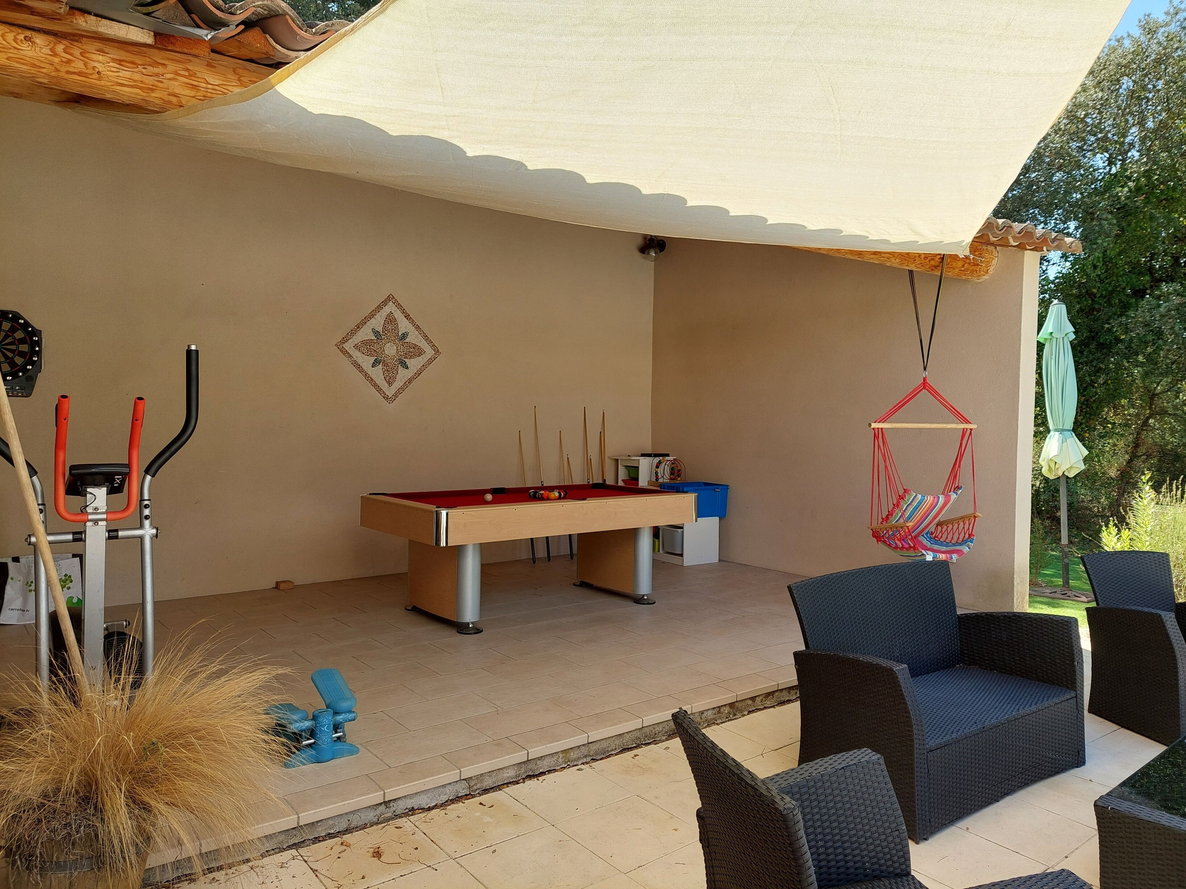 A pool table, exercise equipment, and outdoor seating in a covered patio area.