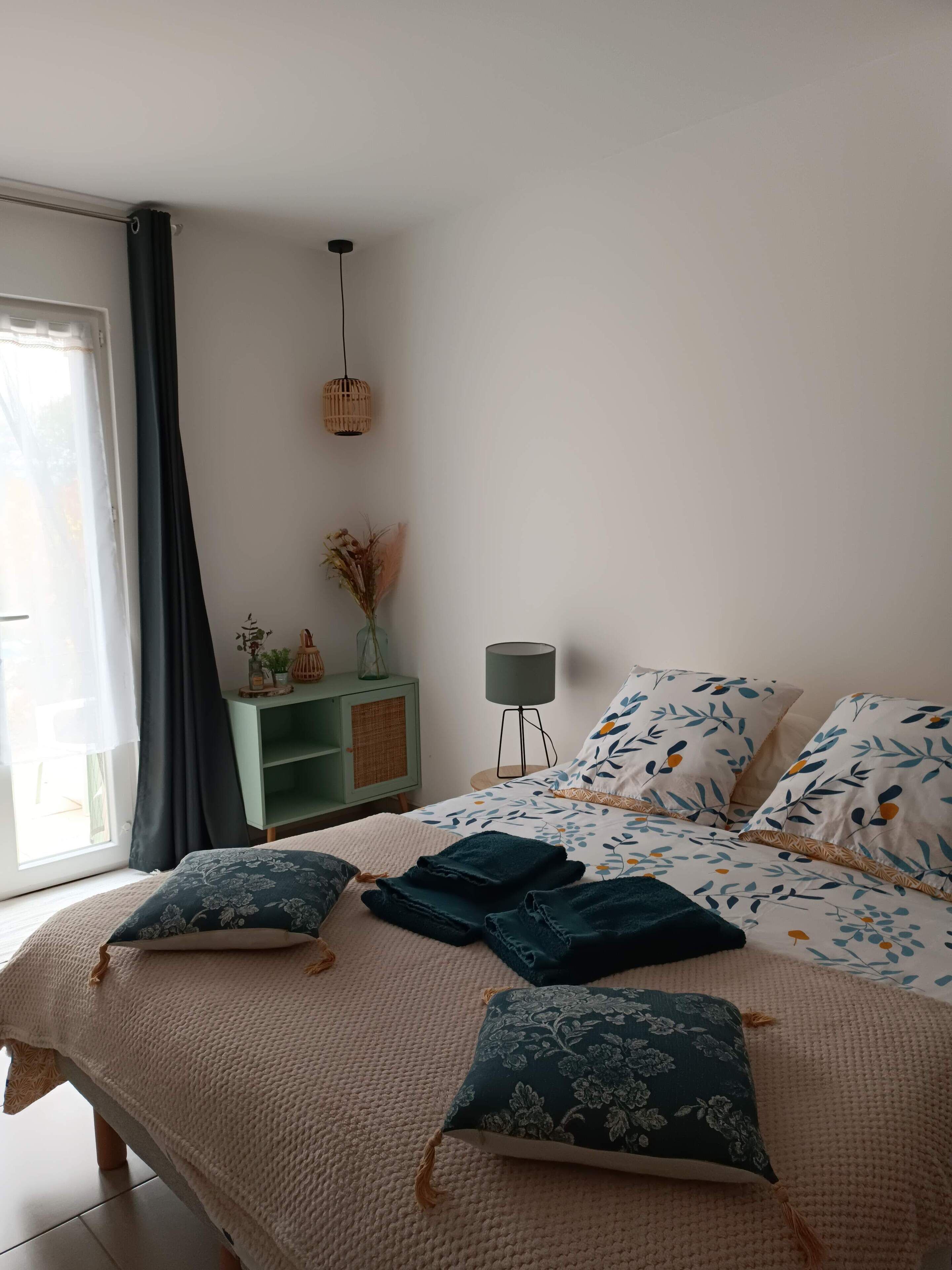 A bedroom with a bed, pillows, a bedside table, a lamp, and a window with curtains.