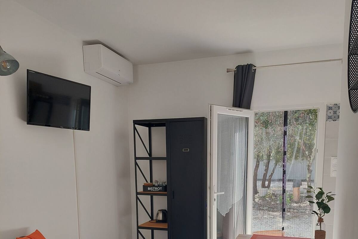 Een slaapkamer met een bed, een stoel, een bureau, een kledingkast, een televisie en een schuifdeur naar een balkon.