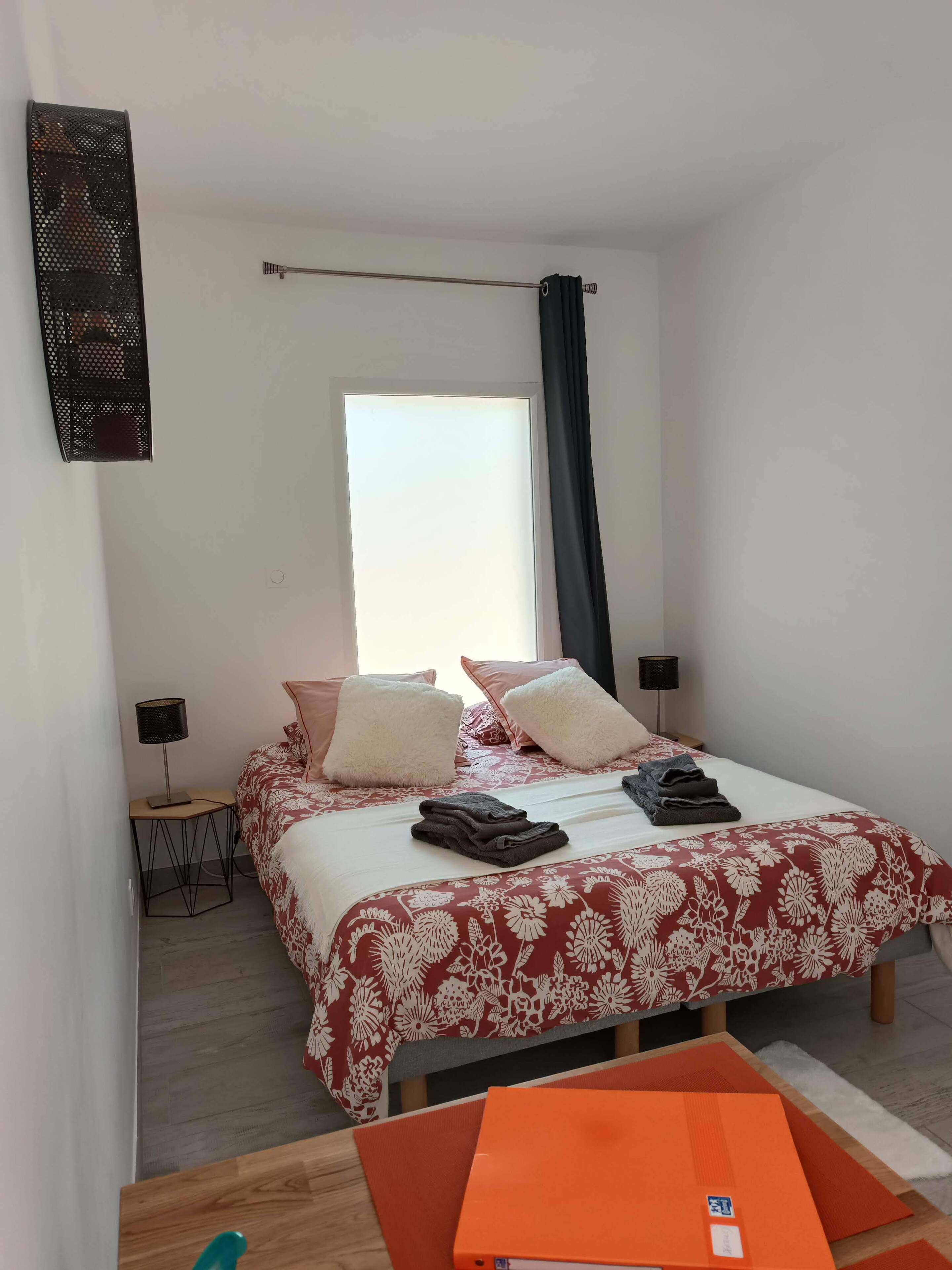 A bedroom with a bed, two bedside lamps, a window with curtains, and a small table with a lamp.