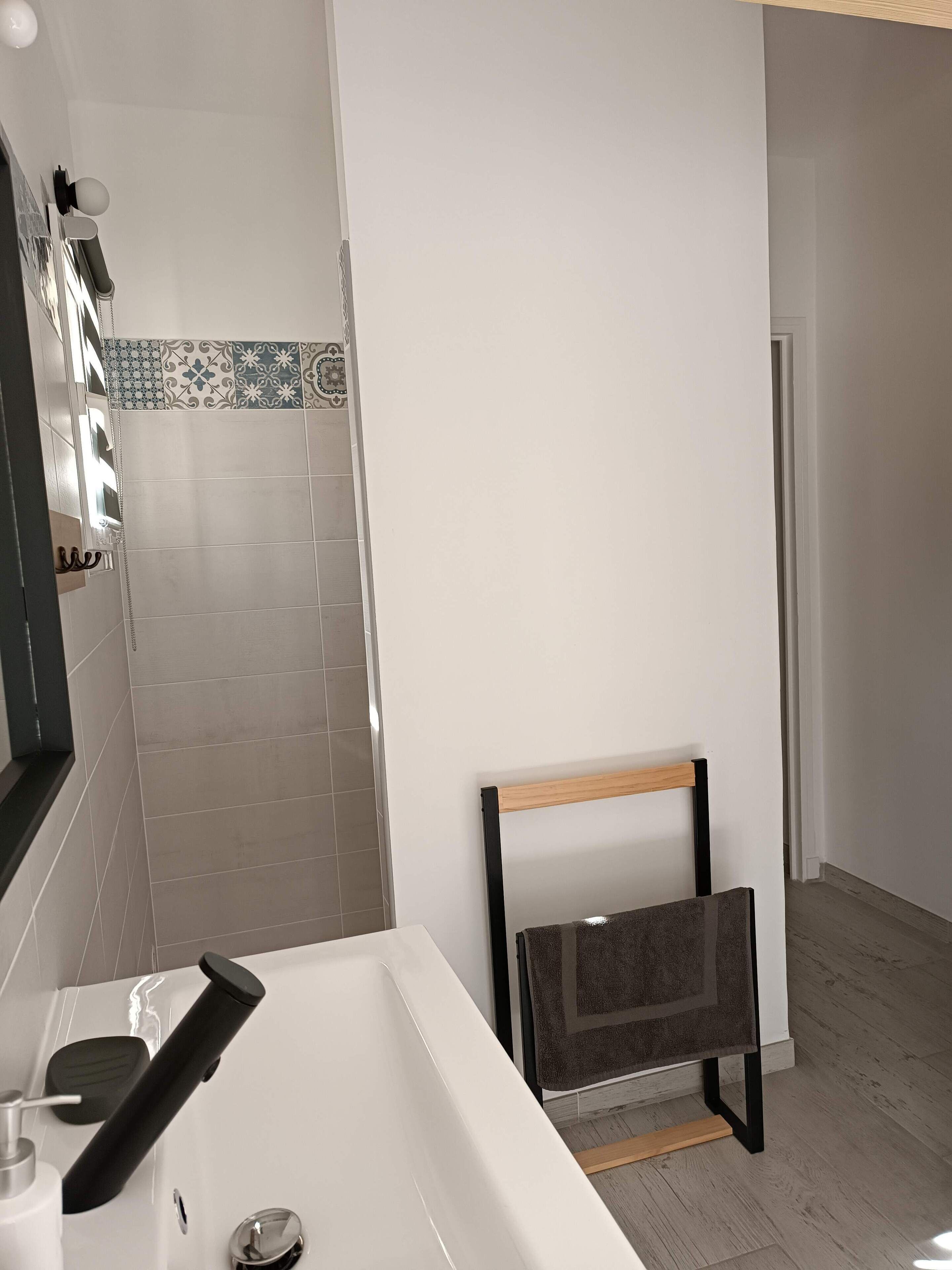 A modern bathroom with a white sink, a mirror, a towel rack, and a shower area.