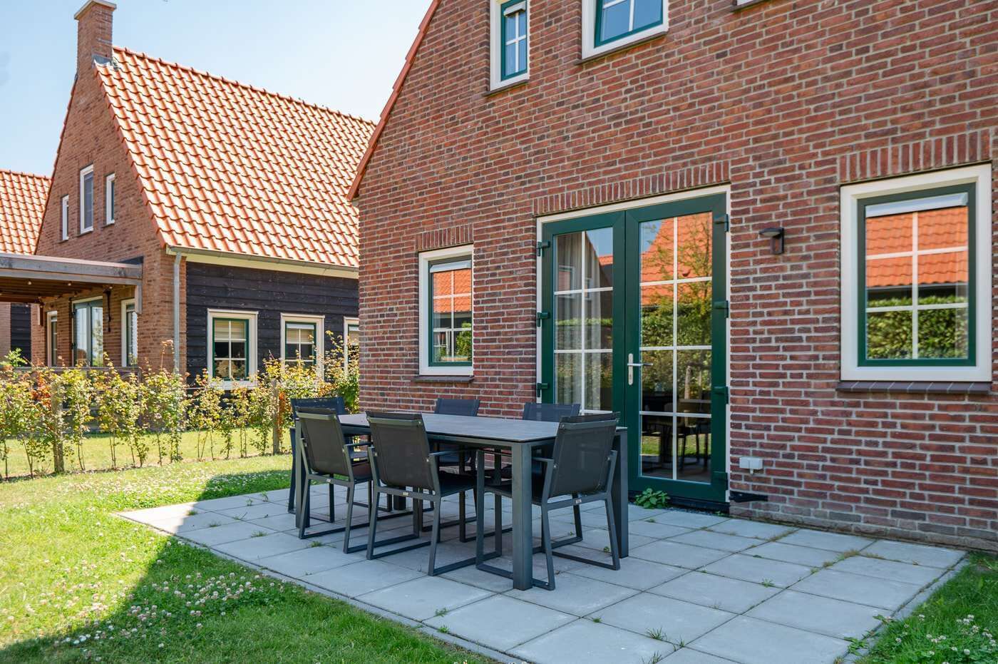 Une maison en briques avec un toit en tuiles, une terrasse avec une table et des chaises, et une porte verte.