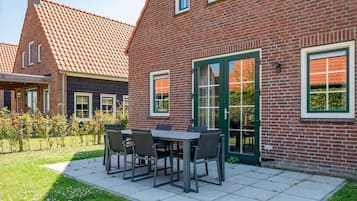 A brick house with a tiled roof, a patio with a table and chairs, and a green door.