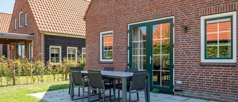 Une maison en briques avec un toit en tuiles, une terrasse avec une table et des chaises, et une porte verte.