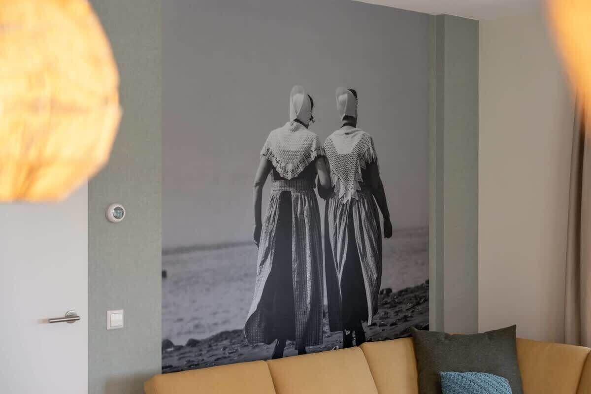 A room with a large black and white photograph of two people on the wall, a sofa with cushions, and a light fixture.