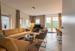 A modern living room with a sofa, coffee table, TV, and dining area.