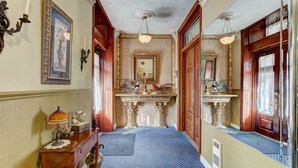 A hallway with a patterned floor, a wooden bench, a table with a lamp, and a mirror above a fireplace. - Cozy 2 bedroom Condo at the Château Sherbrooke, Blend of history & modern luxury (Montréal)