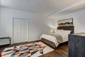 Ein Schlafzimmer mit einem Bett, einem geometrischen Teppich, einem Holzkopfteil, einem Bild an der Wand und einer Heizung.