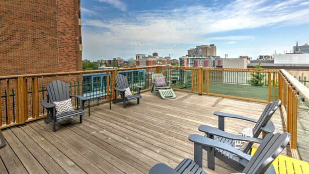 A wooden deck with Adirondack chairs, a brick wall, and a city view. - Cozy 2 bedroom Condo at the Château Sherbrooke, Blend of history & modern luxury (Montréal)
