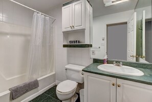 Ein Badezimmer mit Badewanne, Toilette, Waschbecken und weißen Schränken.