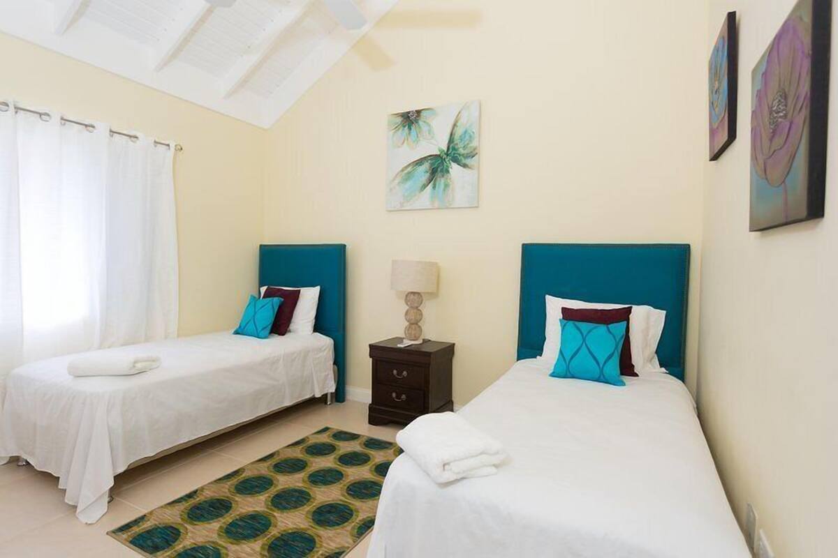 A hotel room with two single beds, a nightstand, a lamp, and artwork on the walls.