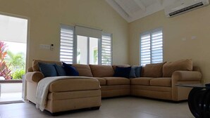 Una sala de estar con un sofá seccional color crema, un pequeño reposapiés y una mesa de centro de vidrio.