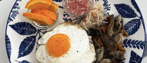 A plate with a fried egg, rice, dried fish, and a small bowl of diced onions.