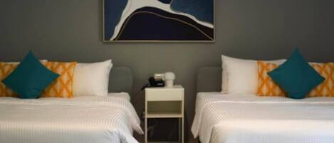 A hotel room with two beds, each with a pillow and a small bedside table.