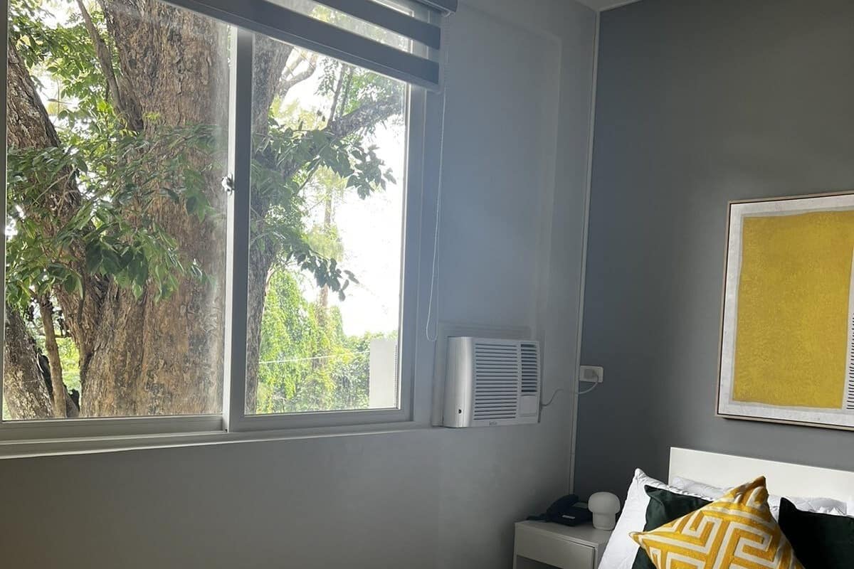 A bedroom with a bed, a nightstand, a wall-mounted air conditioner, and a window with blinds.