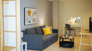 Ein modernes Wohnzimmer mit einem grauen Sofa, einem gelben Kissen, einem kleinen weißen Tisch und einem Schreibtisch mit einem Stuhl.