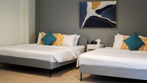 Ein Hotelzimmer mit zwei Betten, jeweils mit weißer Bettwäsche und türkisblauen Kissen. An der grauen Wand hängt ein großes, abstraktes Gemälde über den Betten.