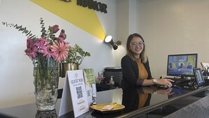 Ein Empfangsschalter mit einem Schild, auf dem 'EMERALD MANOR' steht. Auf dem Schalter befinden sich eine Vase mit Blumen, ein Schild mit einem QR-Code und ein Computermonitor.