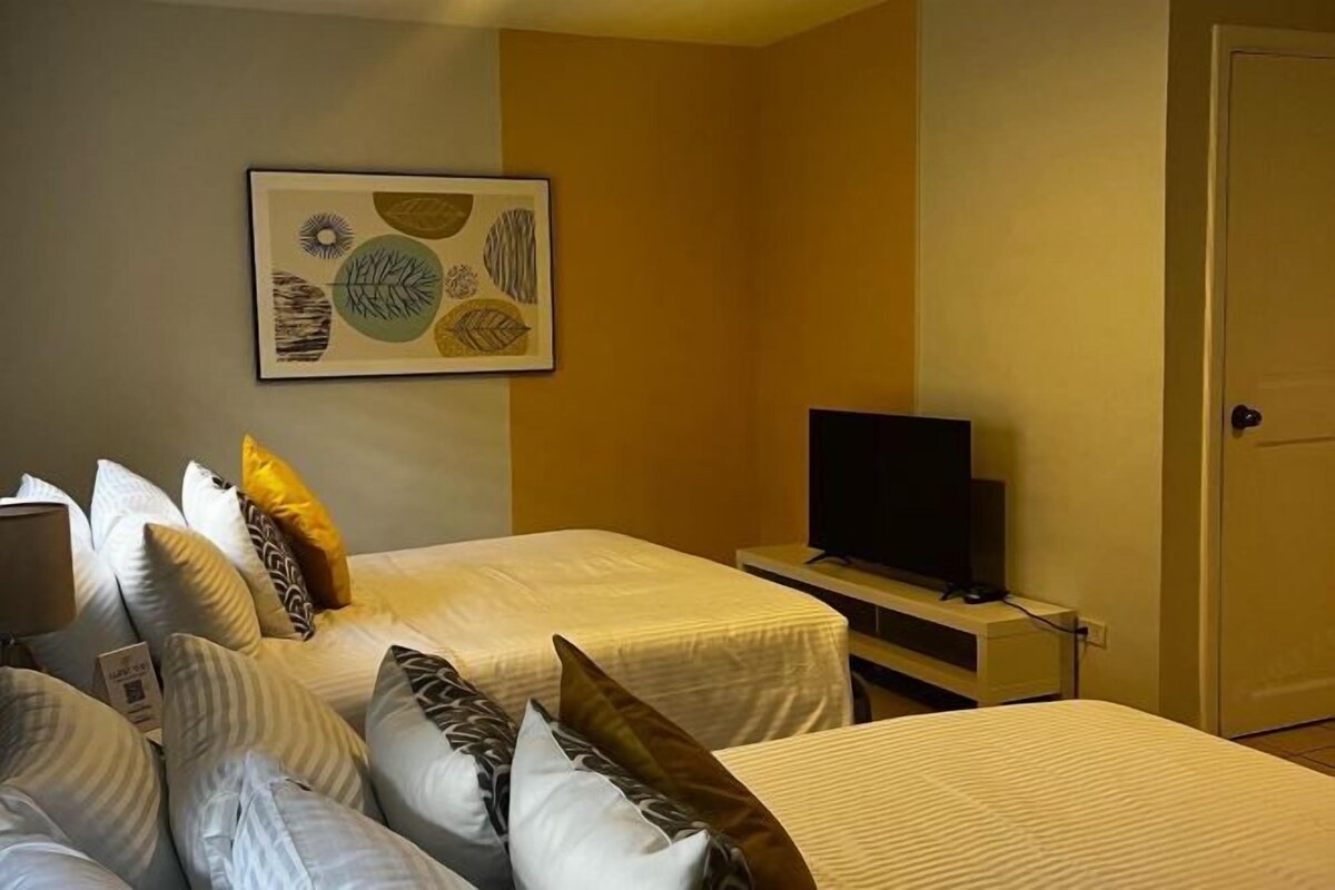 A hotel room with two beds, a television on a stand, and a framed artwork on the wall.