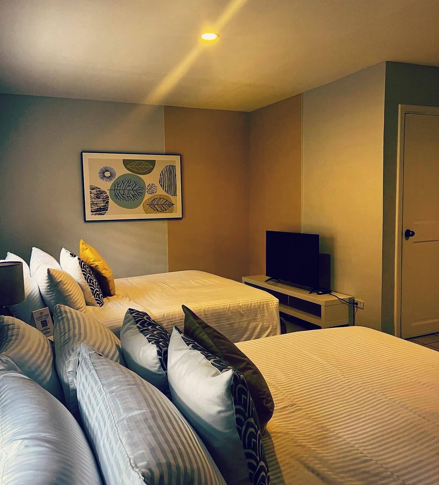 A hotel room with two beds, a flat-screen TV, a framed artwork on the wall, and a door.