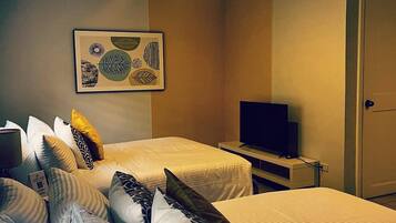 A hotel room with two beds, a flat-screen TV, a framed artwork on the wall, and a door.
