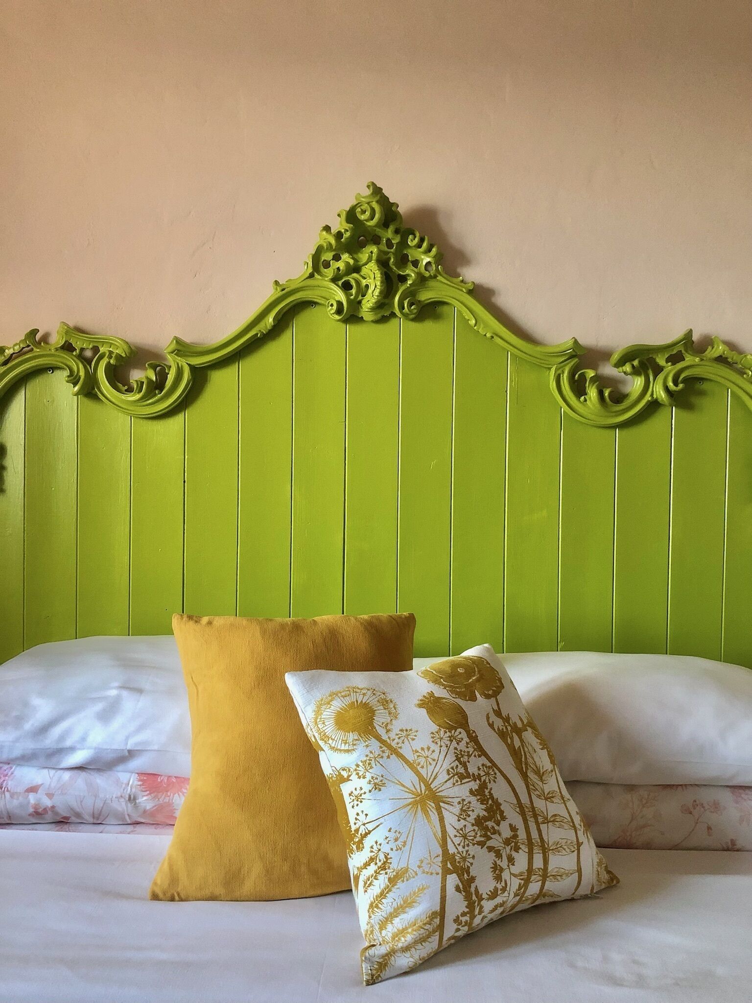 A bed with a green headboard and two pillows, one yellow and one with a floral pattern.