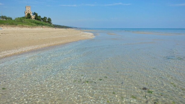 A beach with clear shallow waters, a sandy shore, and a tower-like structure in the background. - Ephemeral - Relaxing Retreat (Abruzzo)