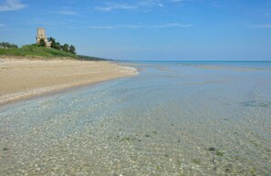 A beach with clear shallow waters, a sandy shore, and a tower-like structure in the background. - Ephemeral - Relaxing Retreat (Abruzzo)